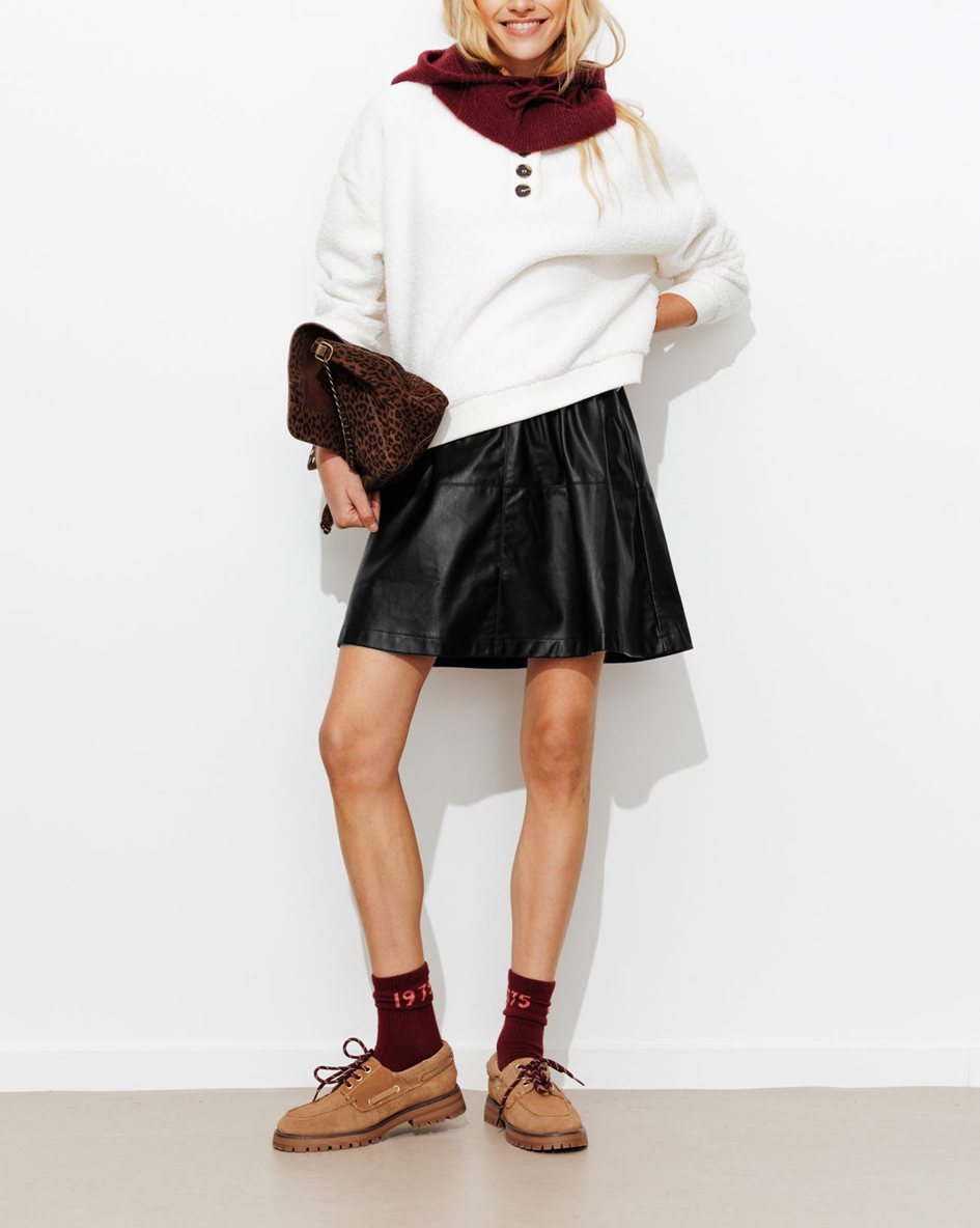 mannequin portant une jupe courte en simili, avec un pull, une cagoule et un sac léopard