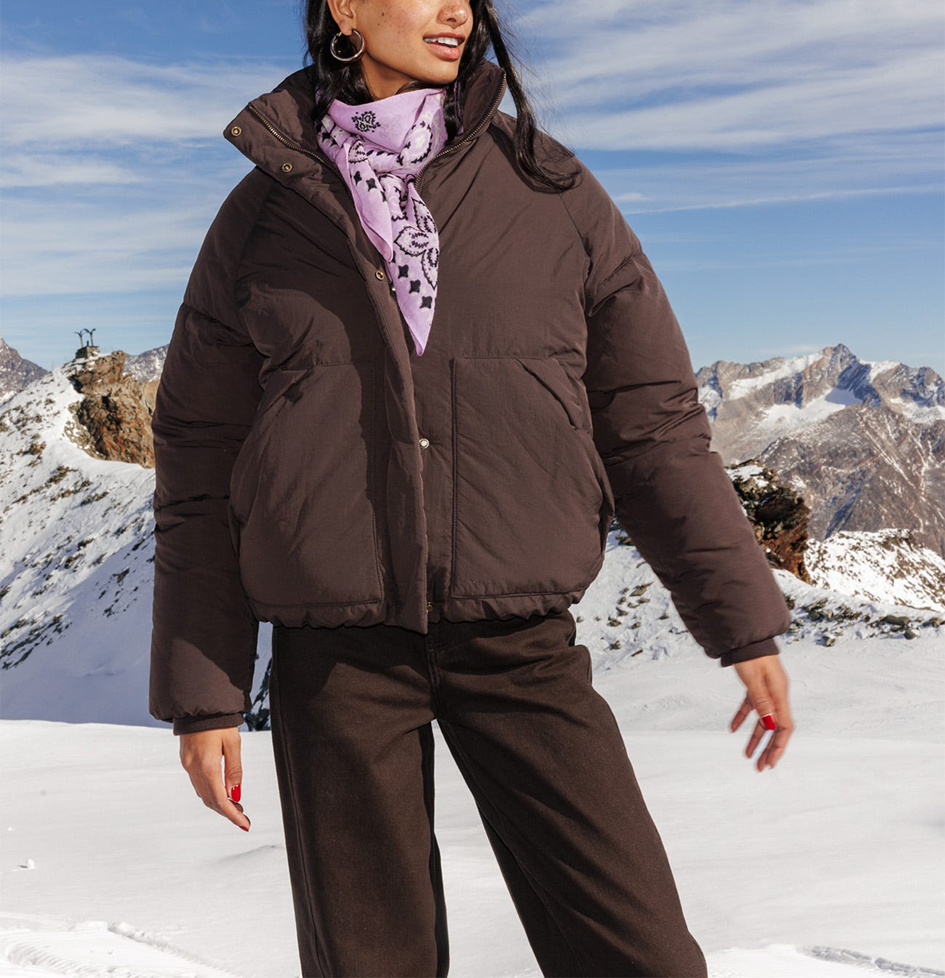 Mannequin portant une doudoune marron uni, avec un pantalon marron et un foulard 