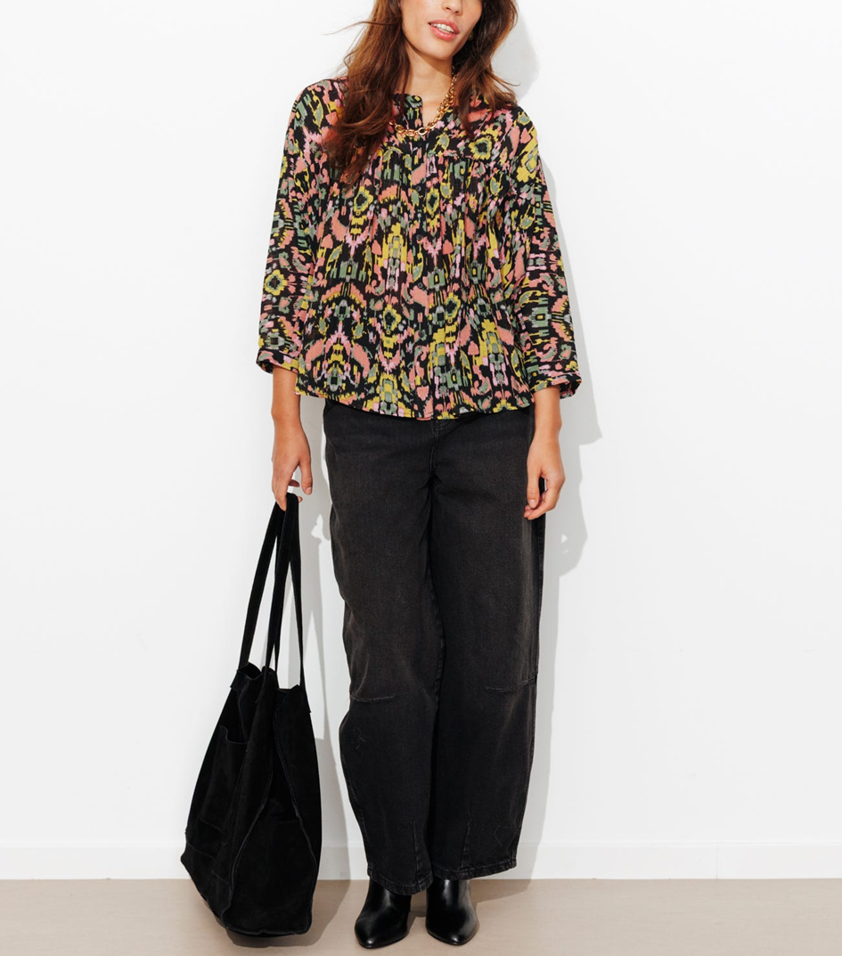 mannequin portant une blouse arty avec un pantalon noir et un sac noir