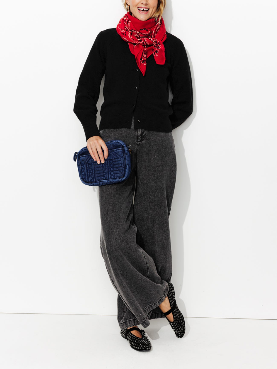 mannequin portant un look monochrome noir, accessoirisé par un foulard rouge et un sac en denim bleu  