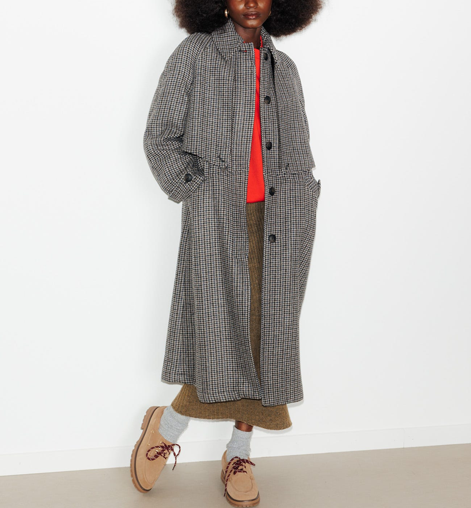 mannequin portant un trench à motif avec en dessous un pull rouge et une jupe en maille longue 