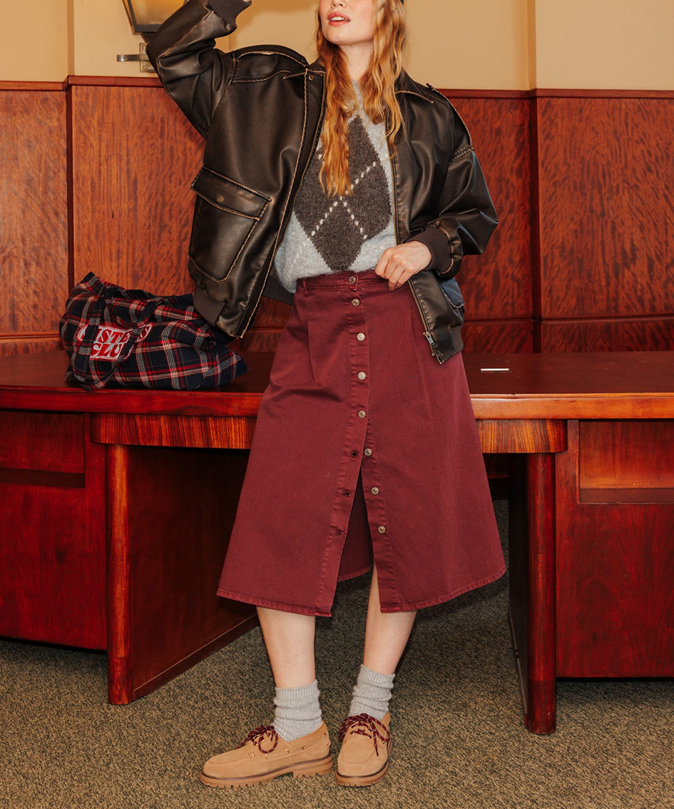 mannequin portant une jupe midi bordeau en jean avec une veste en cuir marron 