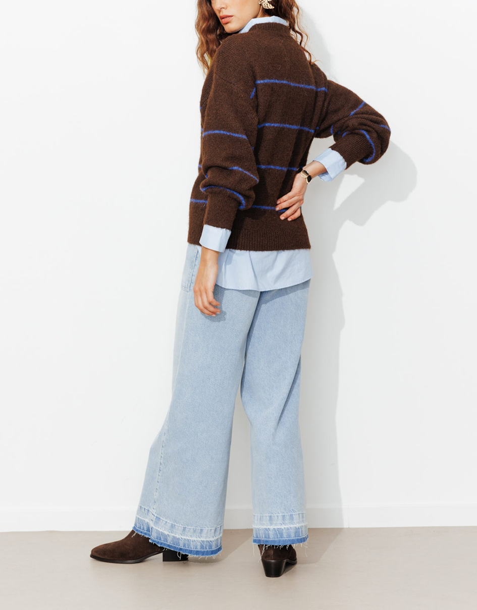 mannequin portant un pull marron accordé avec des bottes marrons et un jean et une chemise bleu