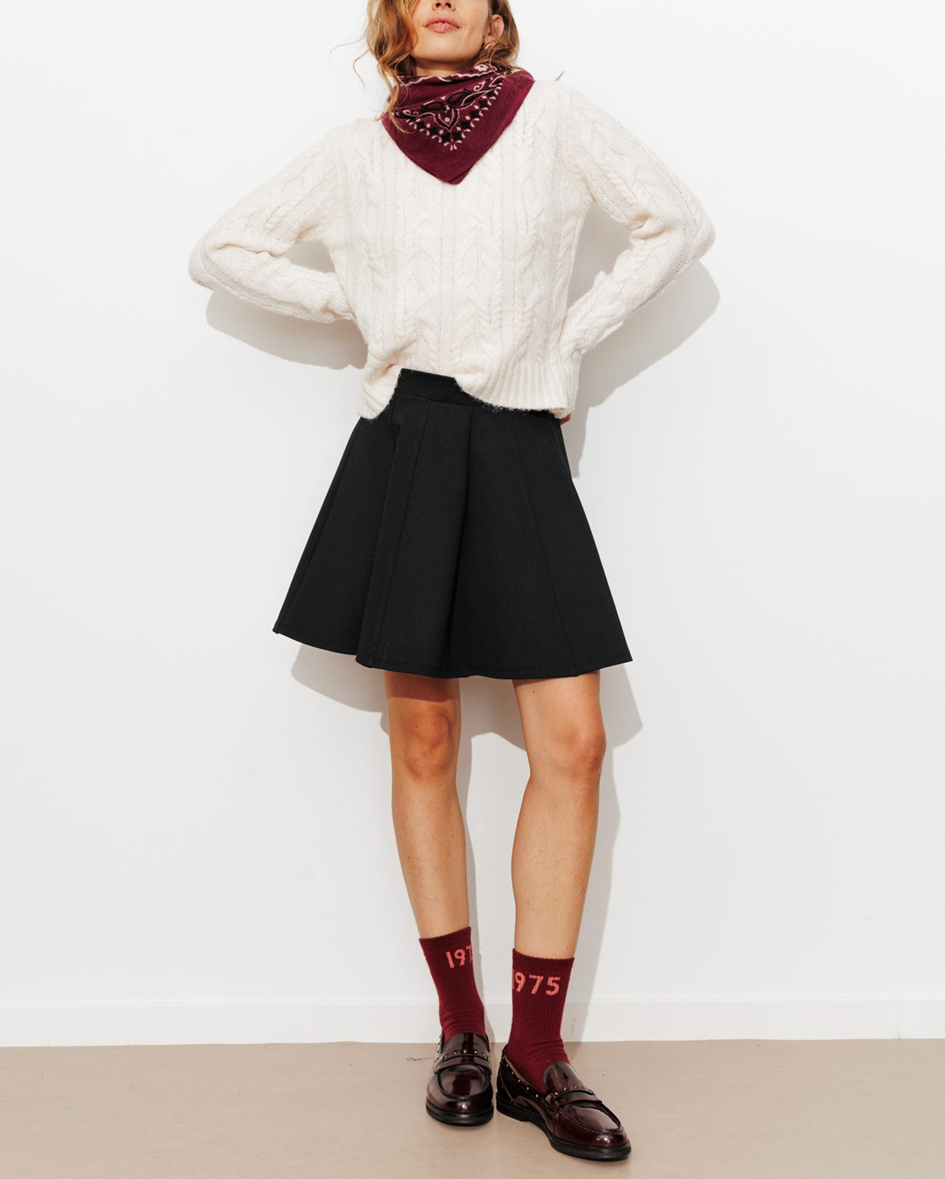 mannequin portant une jupe noire courte avec un pull oversize blanc rentré sur le devant 