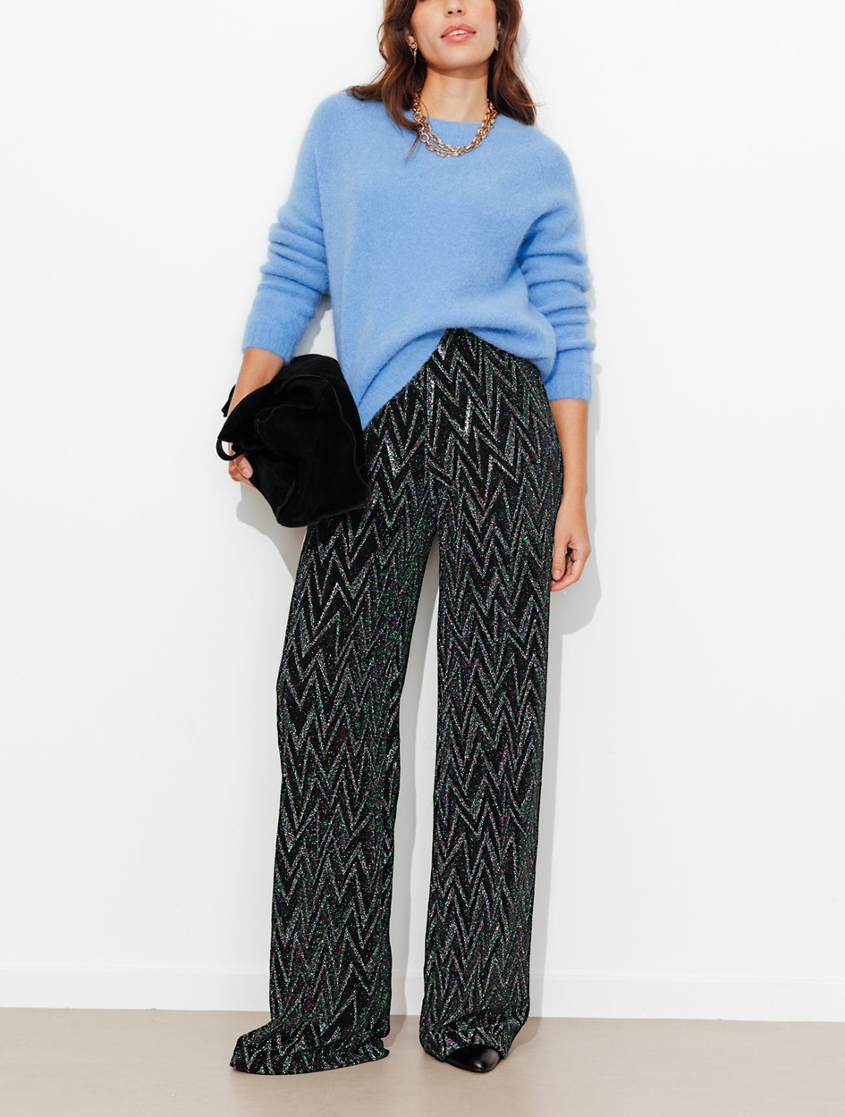 mannequin portant un pantalon à paillettes effet zig zag, avec un pull, un collier, un sav 