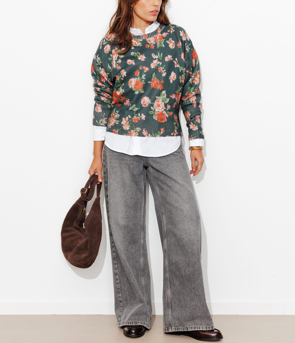 mannequin portant un pull à fleurs sur fond noir ave une chemise blanche en dessous, un jean