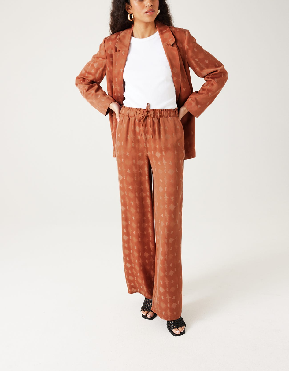 mannequin portant un ensemble tailleur en satin en terre de sienne avec un t-shirt blanc en dessous et des sandales noires 