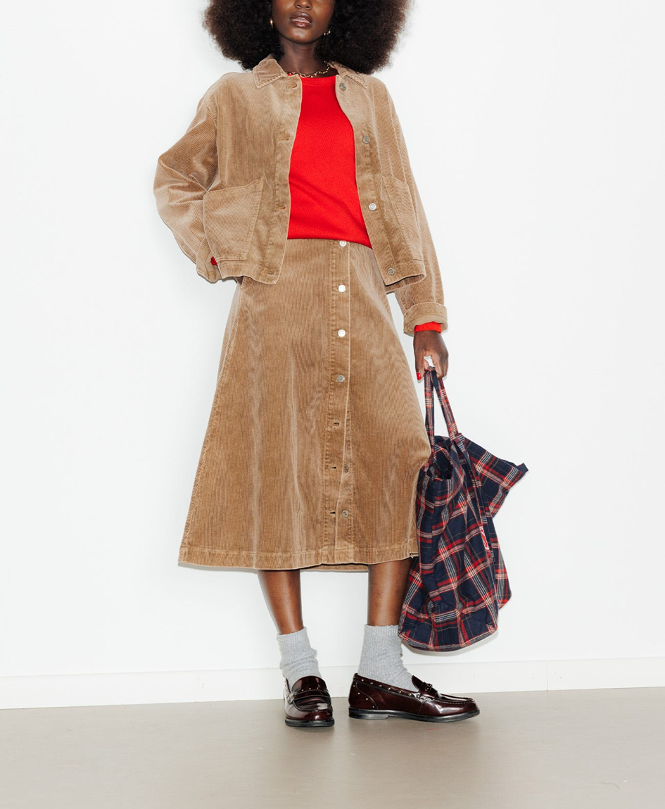 mannequin portant une jupe midi en velour avec un sweat rouge et une veste en velour, portant un sac tôt bag en laine à carreau 