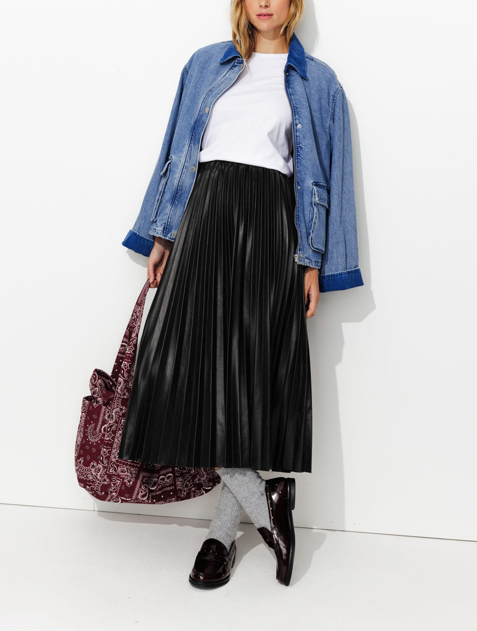 mannequin portant une jupe midi plissée en simili cuir avec un t-shirt une une veste en jean par dessus. Portant un sac tote bag à la main et des mocassins 