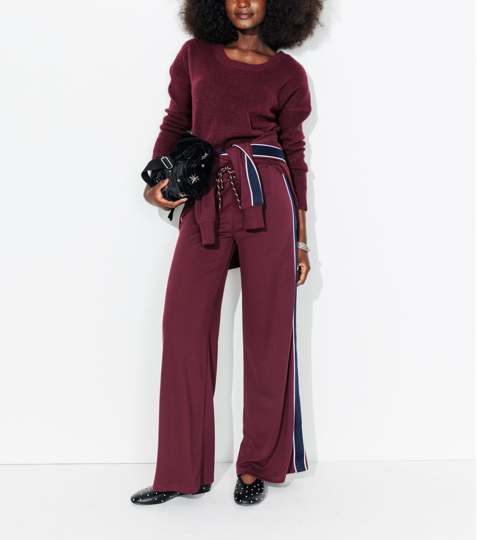 mannequin portant un look monochrome bordeaux dont un pull à longue manches, un pantalon large et une veste autour de sa taille, avec un sac 